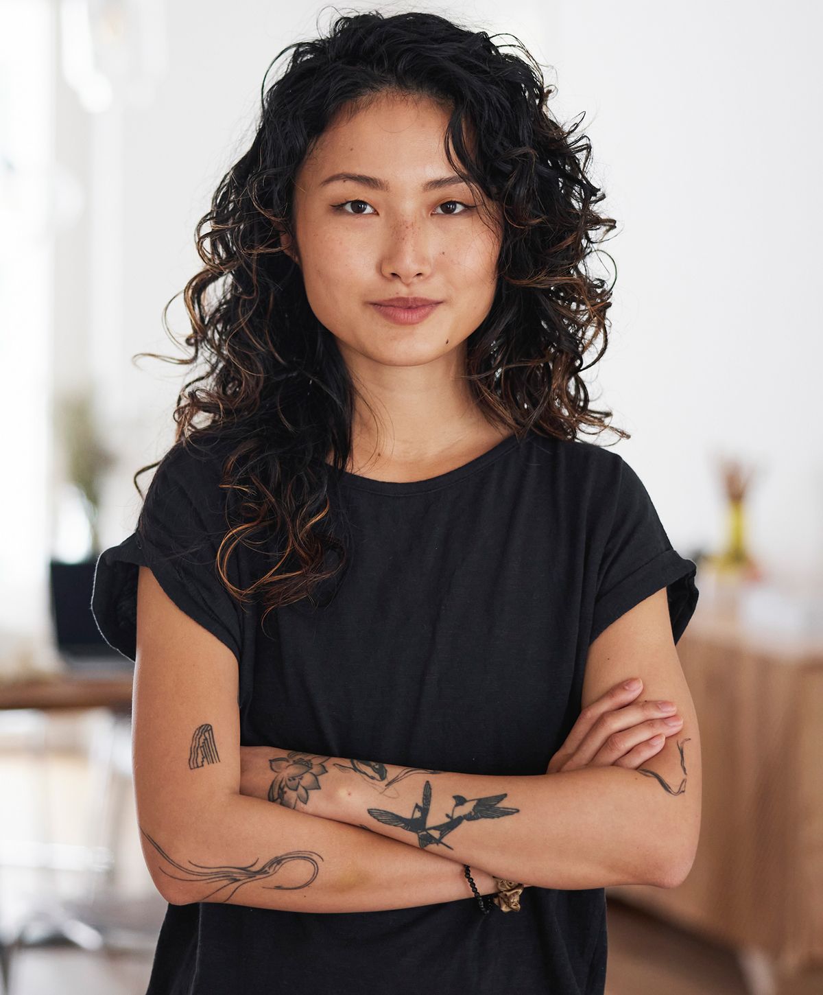 Confident person with curly hair and tattoos.