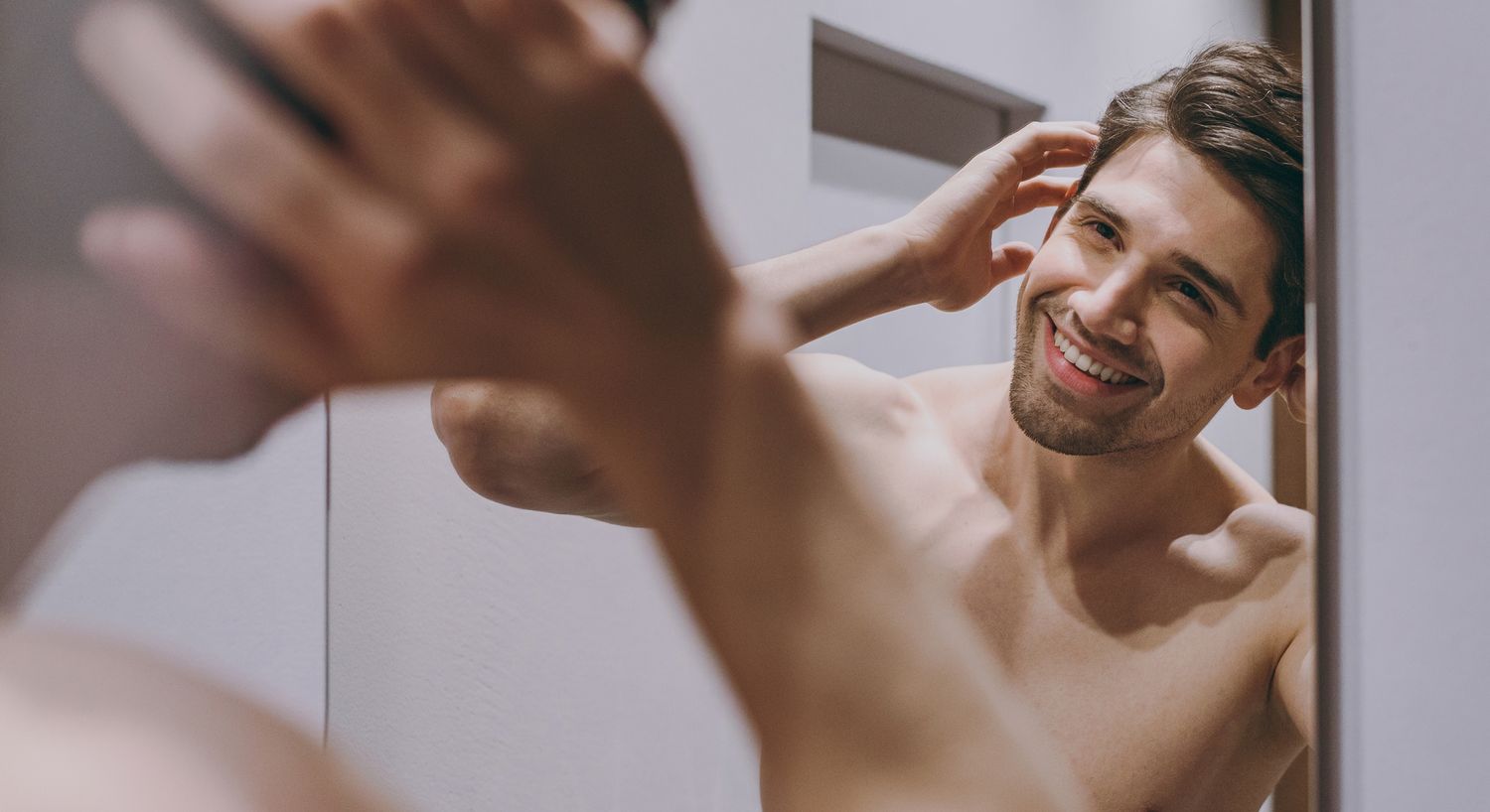 Man grooming and smiling in bathroom mirror