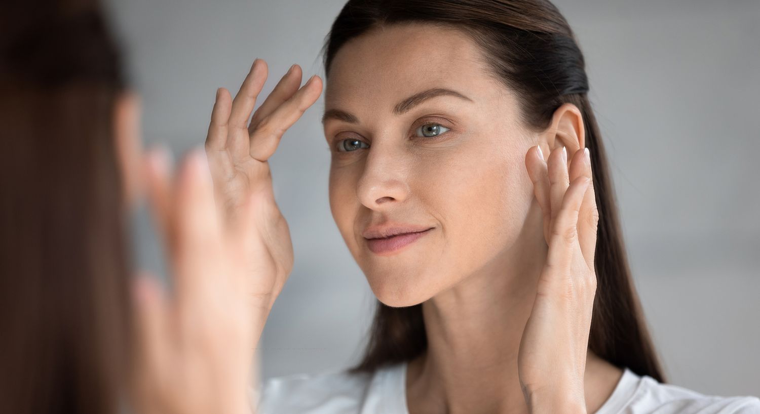 Woman applying skincare in front of a mirror.
